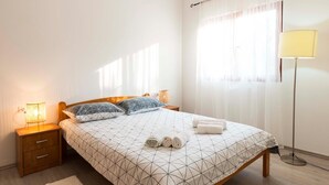 A neatly made bed with a geometric patterned bedspread, two pillows, and rolled towels on a wooden floor. - 2 bedroom lovely apartment in Bale (Bale)