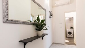 A hallway with a decorative mirror, a potted plant on a black shelf, and a washing machine in the background. - 2 bedroom lovely apartment in Bale (Bale)