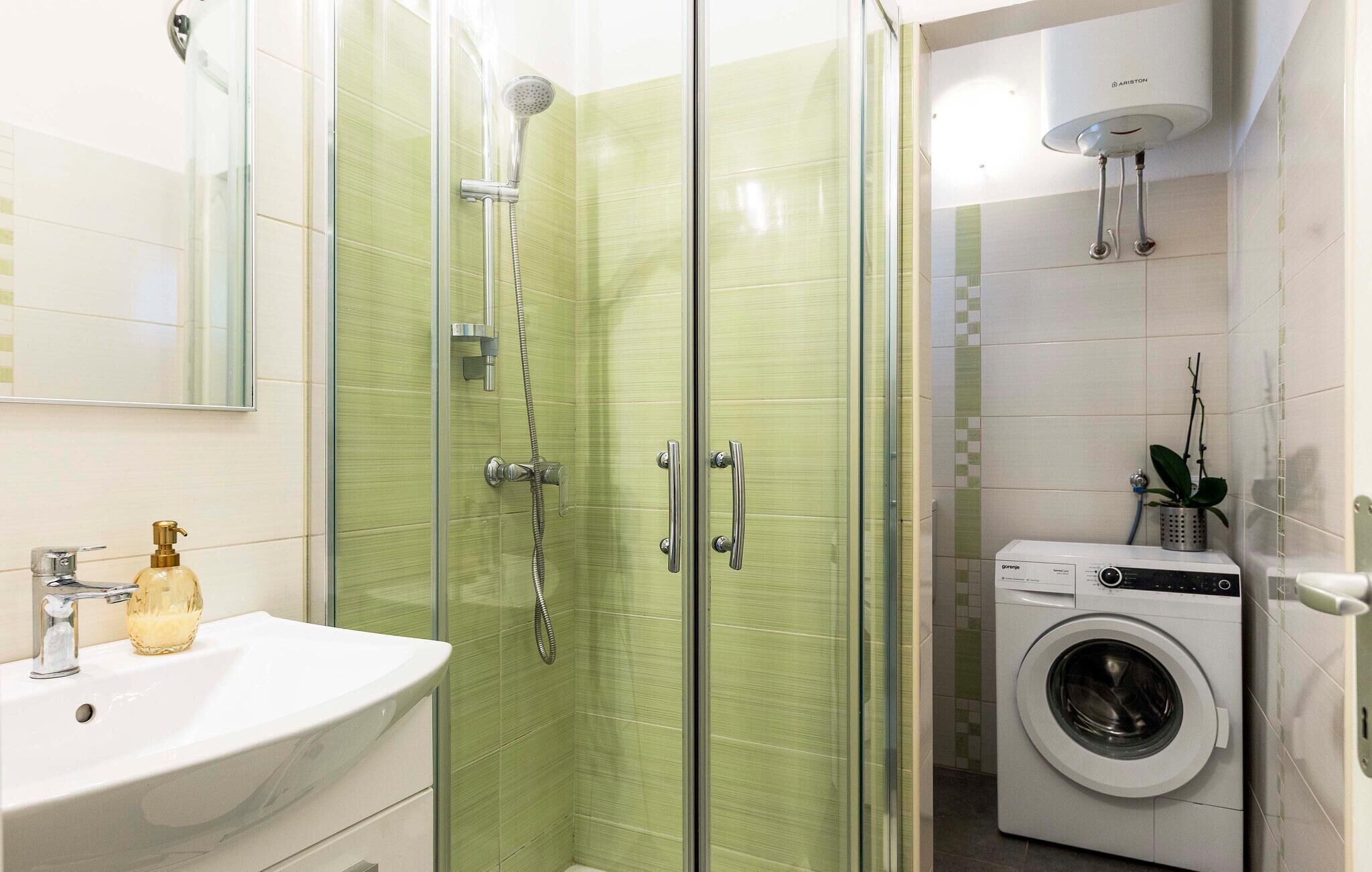 A modern bathroom with a glass-enclosed shower, a sink with a soap dispenser, and a washing machine.