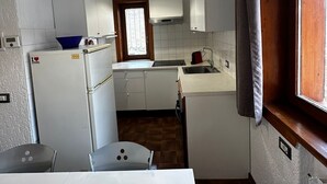 A compact kitchen with white cabinets, a built-in oven, a sink, and a window with curtains. - La Finestra Su Livigno, House with a View (Teola)
