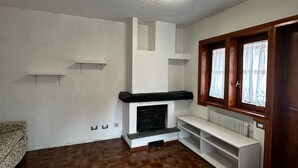 A room with a fireplace, wooden floor, white walls, and a window with curtains. - La Finestra Su Livigno, House with a View (Teola)