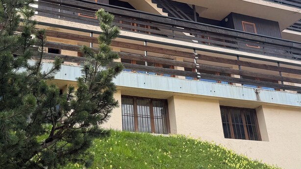 A multi-story building with balconies, a staircase, and a grassy area with yellow flowers. - La Finestra Su Livigno, House with a View (Teola)