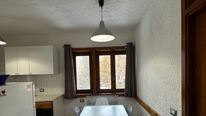 A compact kitchen with a dining table, white cabinets, a refrigerator, and a window with curtains. - La Finestra Su Livigno, House with a View (Teola)
