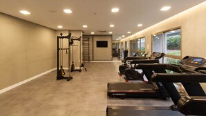 A gym with treadmills, weight machines, and a wall-mounted TV. - Studio com Varanda a 280m do Metr Vila Madalena (São Paulo)