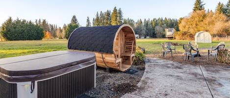 A hot tub and wooden barrel structure in a backyard with outdoor seating and a shed in the background.