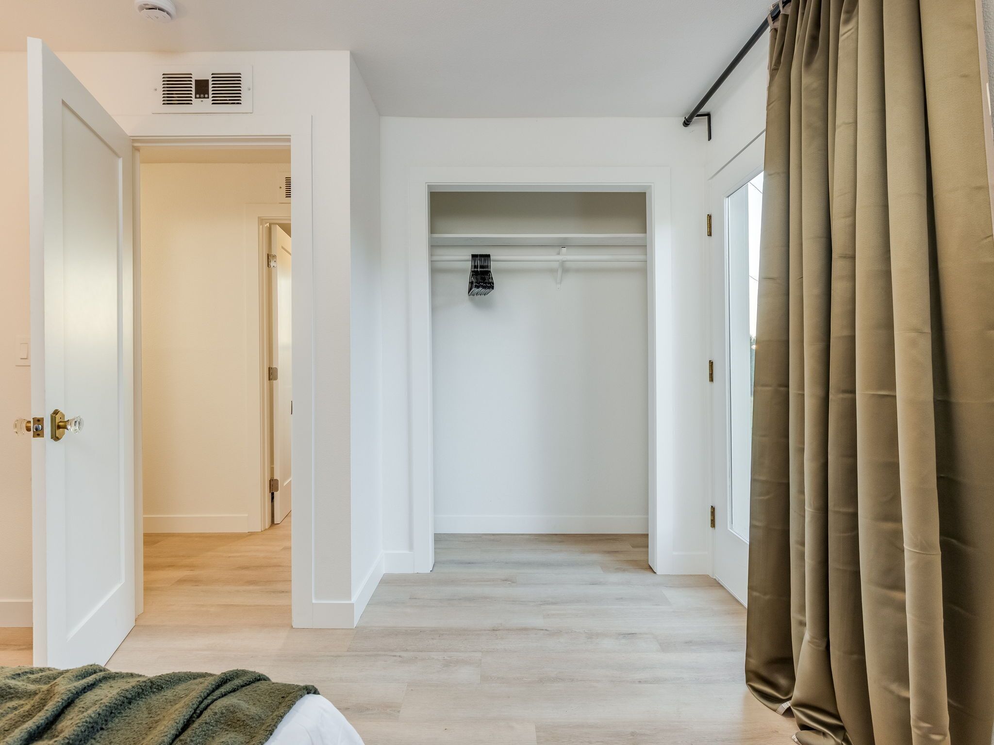 Un couloir avec une porte blanche sur la gauche, un rideau marron sur la droite et un placard avec une tringle à vêtements au centre.
