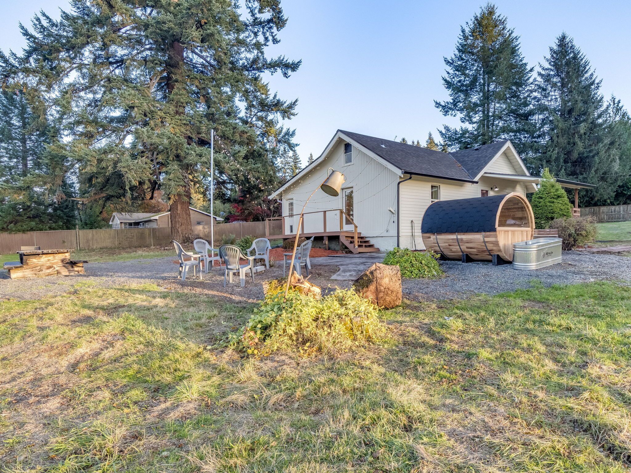 A house with a sauna, outdoor seating, and a large tree in the backyard.