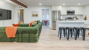 A modern living room with a green sofa, a flat-screen TV, and a kitchen with white cabinets and stainless steel appliances. - SPA&Sauna Retreat-Serene Setting, picnic/fireplace, Enjoy with the whole family! (Vancouver)