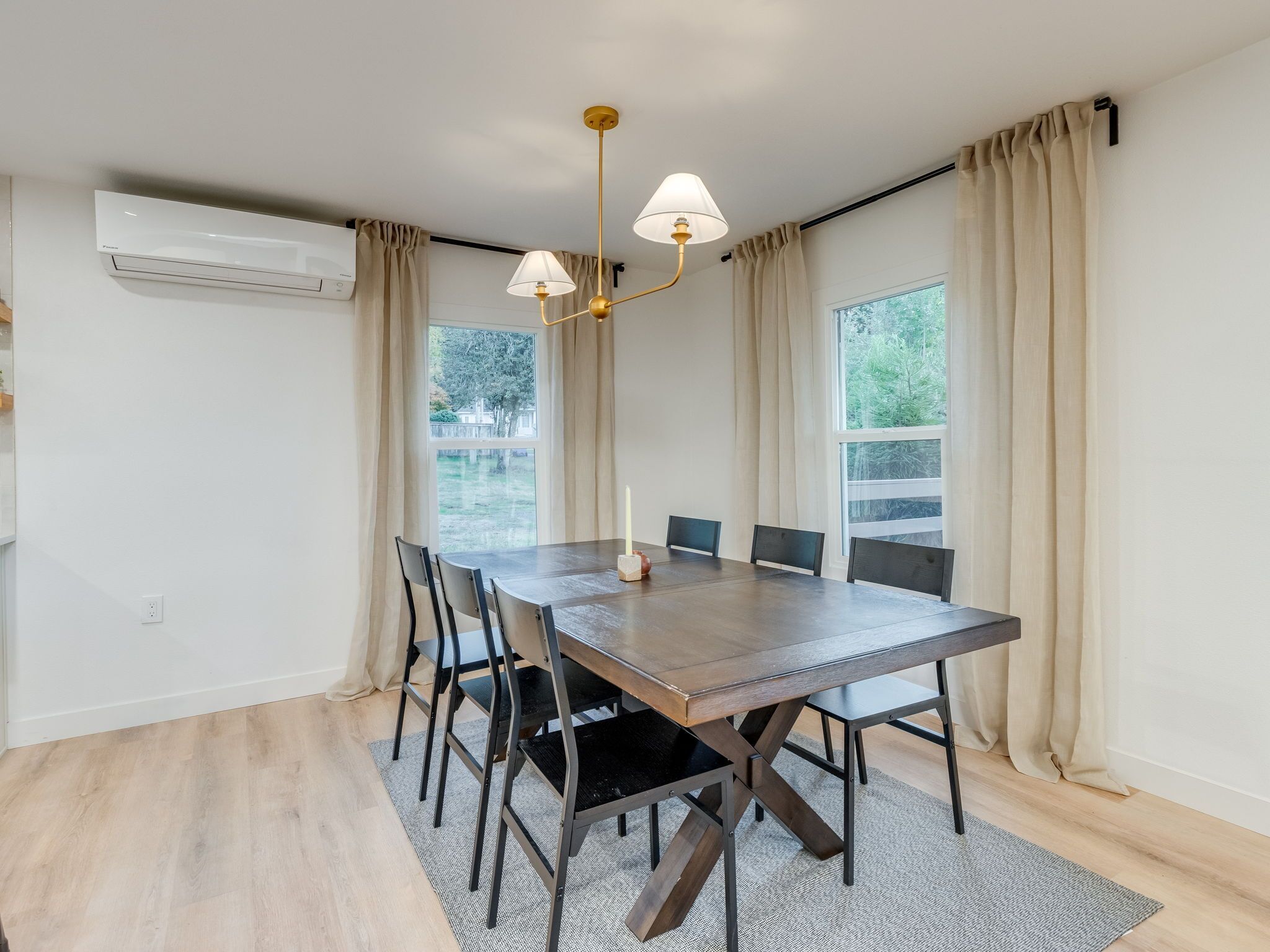 A dining area with a wooden table, black chairs, a chandelier, and large windows with curtains.
