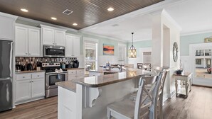 A modern kitchen with white cabinetry, stainless steel appliances, and a central island with bar seating. - Cobia Cabana (Destin)