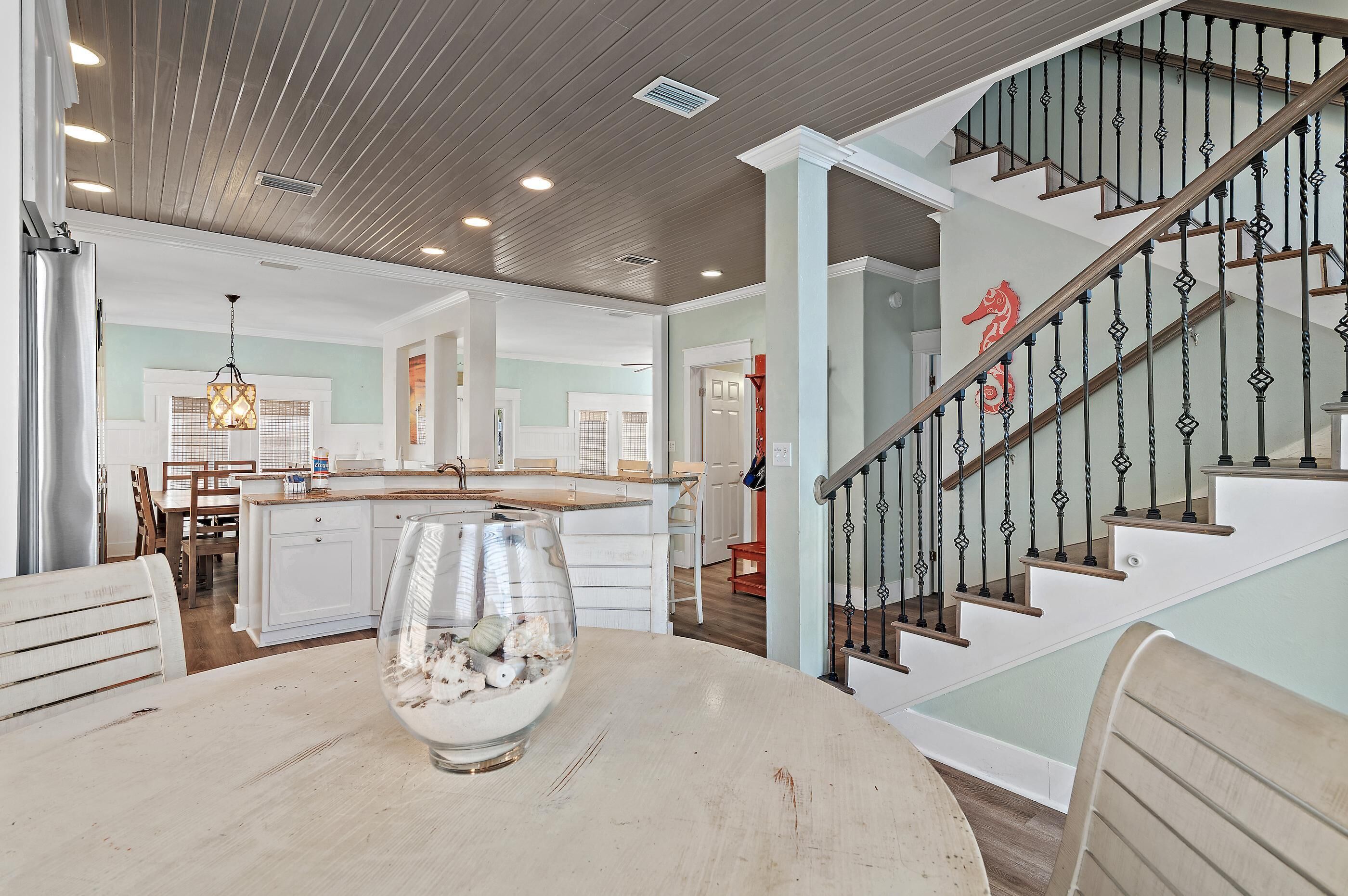 A spacious kitchen with a central island, a dining area with a round table, and a staircase with a decorative railing.