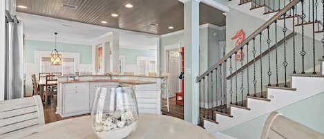 A spacious kitchen with a central island, a dining area with a round table, and a staircase with a decorative railing.