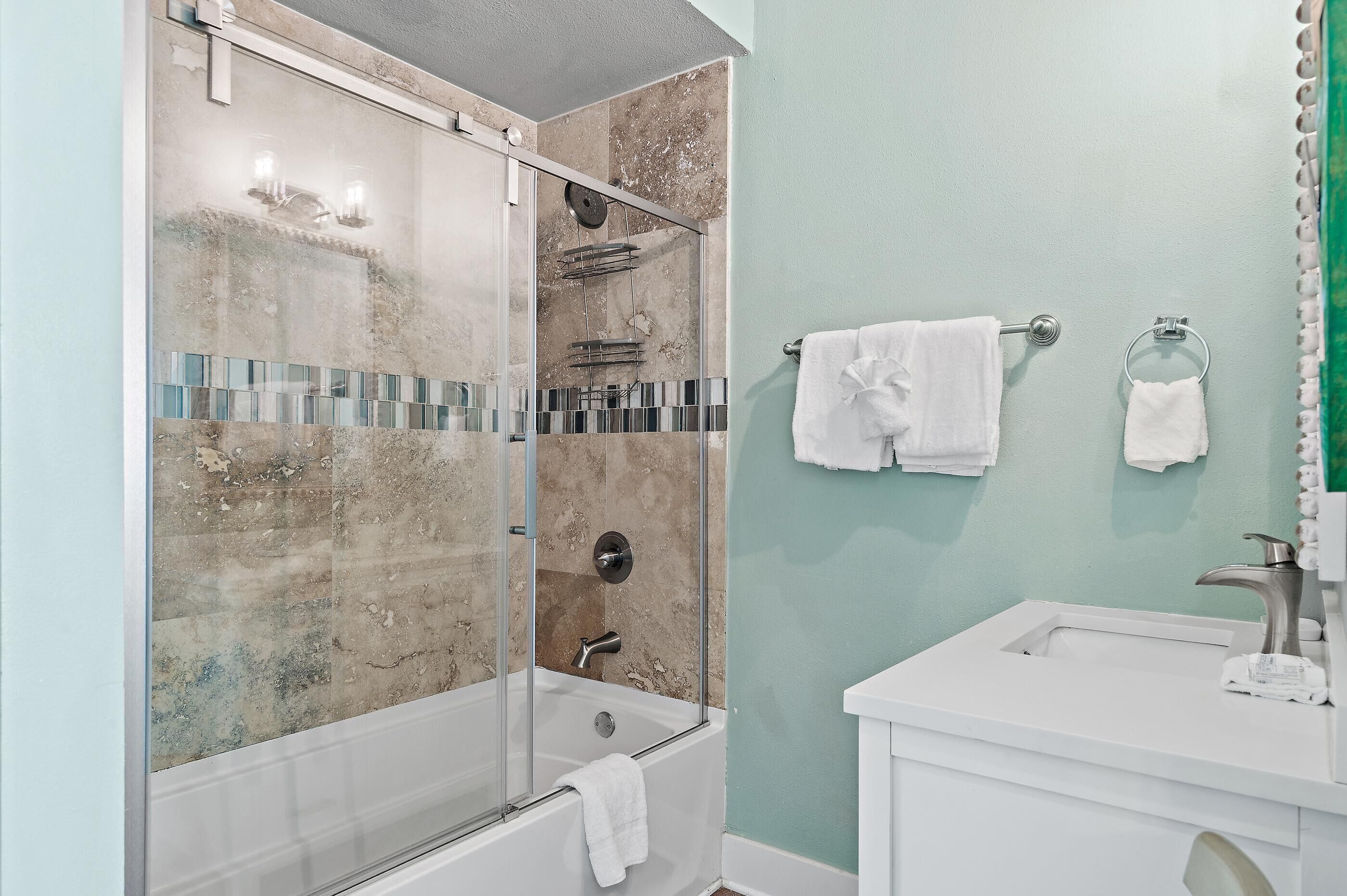 Un baño con ducha de vidrio, bañera, lavamanos con espejo y dos toallas colgadas en la pared.