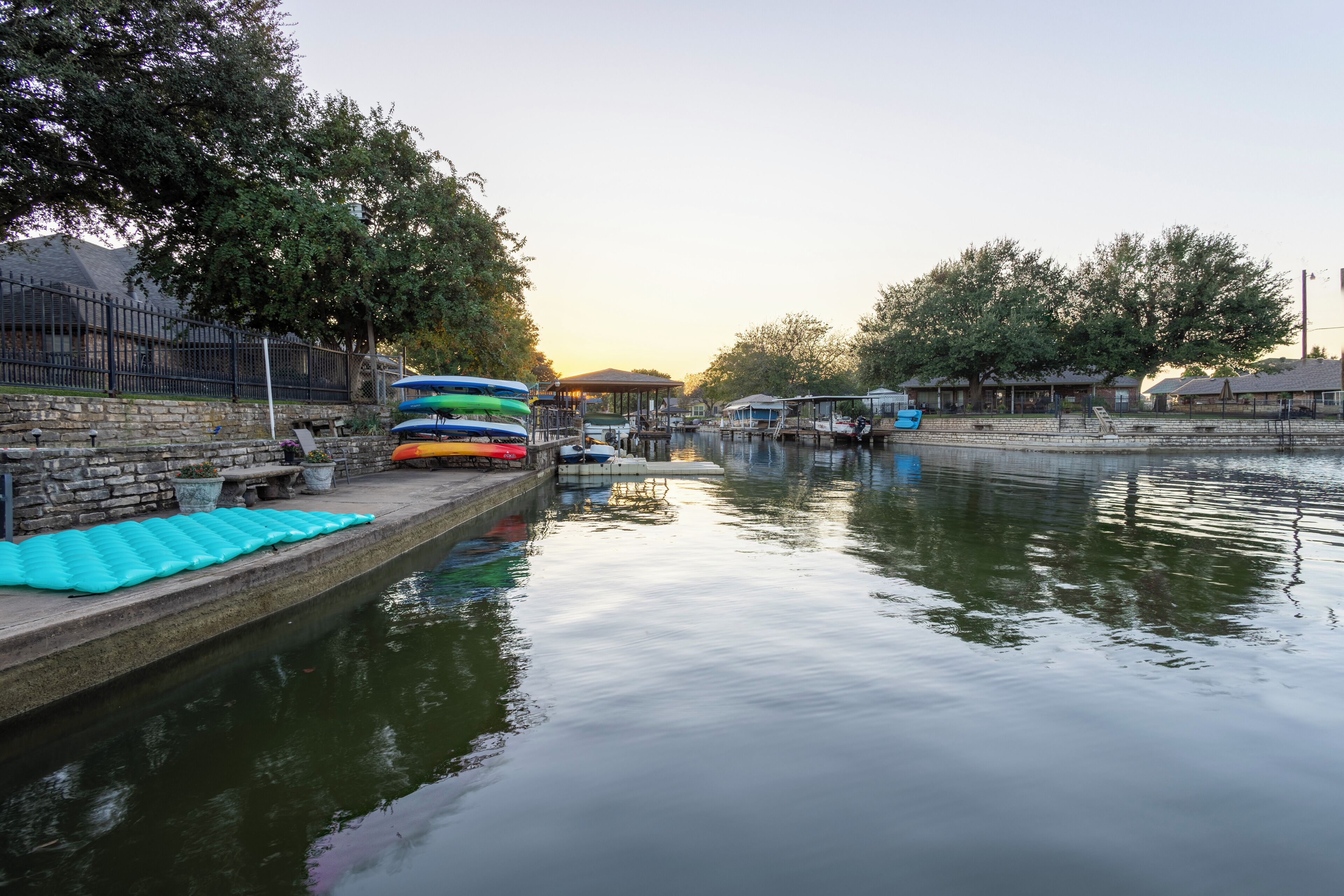 Um rio calmo com barcos e caiaques atracados nas margens.