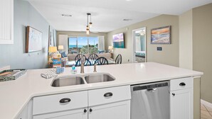 A modern kitchen with a white countertop, stainless steel sink, and dishwasher. - Amalfi Coast 318b (Miramar Beach)