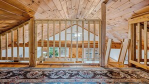 A spacious attic room with wooden beams, a large window, and a patterned rug.
