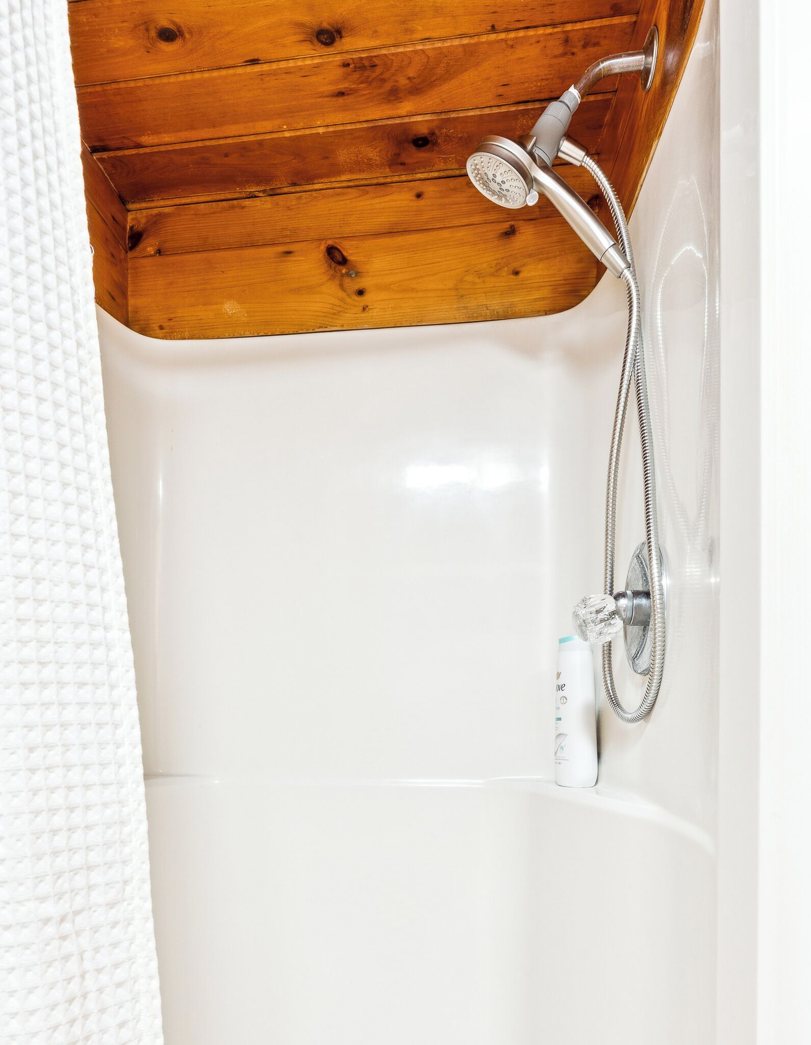 A white bathtub with a showerhead and hose, wooden ceiling beams, and a white towel.