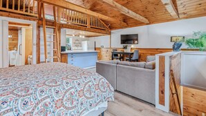 A spacious room with a large bed, a sofa, a dining table, and a kitchen area.