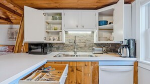 A compact kitchen with white cabinets, a stone backsplash, and a wooden ceiling.