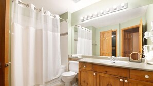 Ein Badezimmer mit Duschvorhang, Toilette, Waschtisch mit Spiegel und Waschbecken.