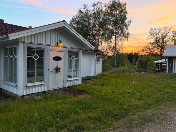 Ein weißes Holzhaus mit geneigtem Dach, einer Haustür und einer kleinen Veranda.