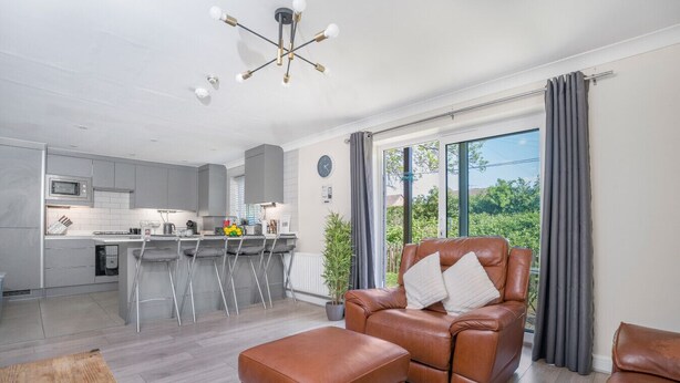 Una sala moderna con un sofá de cuero, una mesa de centro de madera y una zona de cocina con taburetes de bar.