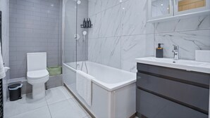 Un baño moderno con ducha, inodoro y lavamanos, con paredes de mármol y piso de baldosas.