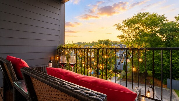 Un balcon agrémenté de meubles en osier, d’un coussin rouge et de guirlandes lumineuses.
