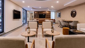 Een moderne woonkamer met een bank, stoelen, een televisie en een eethoek.