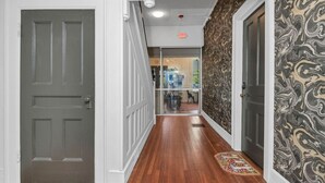 A hallway with a wooden floor, a gray door on the left, and a patterned wall on the right. - Walk to Coffee, Dining & Campus | Historic Studio (Columbia)