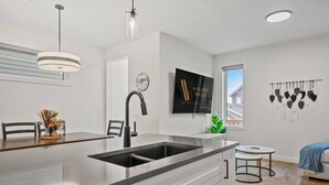 Een moderne keuken met een groot eiland, roestvrijstalen apparatuur en een flatscreen aan de muur.