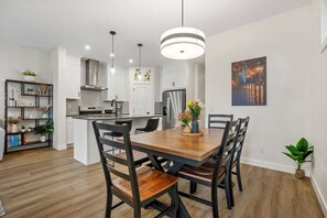 Une cuisine moderne avec des meubles blancs, un îlot central et un coin repas comprenant une table et des chaises en bois.
