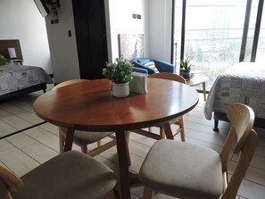 Una sala moderna con una mesa redonda de madera, dos sillones acolchados, un sofá azul y una cama con ropa de cama estampada.
