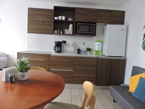 Una cocina moderna con armarios de madera, una encimera blanca, un microondas, una cafetera y un dispensador de agua.