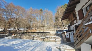 Eine rustikale Holzhütte mit Steinmauern, einer Holzterrasse und verschneitem Gelände.