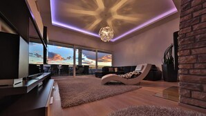 A modern living room with a large TV, comfortable seating, a fireplace, and a view of the sunset through large windows. - Gorgeous home in Podstrana (Podstrana)