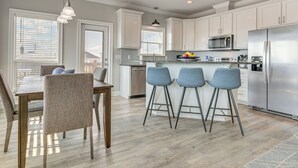 Una cocina moderna con armarios blancos, electrodomésticos de acero inoxidable y una zona de bar con taburetes.