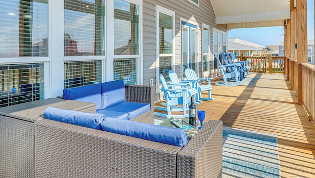 Un espacio al aire libre cubierto con mobiliario de mimbre, cojines azules y una terraza de madera.