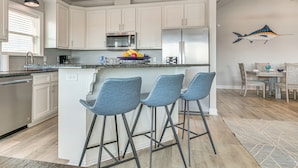 Una cocina moderna con armarios blancos, electrodomésticos de acero inoxidable y una isla central con taburetes de bar.
