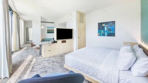 Quarto de hotel moderno com uma cama grande, televisão de tela plana, escrivaninha com cadeira e uma janela ampla com cortinas.