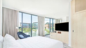 Ett hotellrum med en stor säng, en tv, en stol och utsikt över byggnader och en fontän.