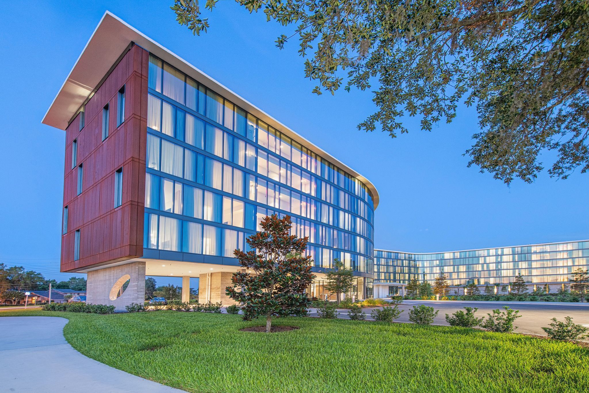 A modern hotel with a curved facade, large windows, and a well-maintained lawn.