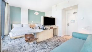 Una habitación de hotel moderna con una cama, un escritorio con una silla, un televisor y un sofá.