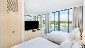 Une chambre d’hôtel avec deux lits, une télévision, un minibar et une grande fenêtre donnant sur un plan d’eau et un espace verdoyant.
