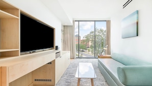 A modern living room with a flat-screen TV, wooden cabinets, a small white table, and a green sofa. - Spacious Lake View Suite near UF Campus (Gainesville)