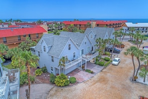 A two-story house with a balcony, surrounded by palm trees and a view of the ocean.