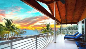 Ein Balkon mit Holzboden, der auf einen Strand im Sonnenuntergang blickt.