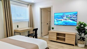 Une chambre d’hôtel avec un lit, un bureau, une chaise, une télévision et une plante en pot.
