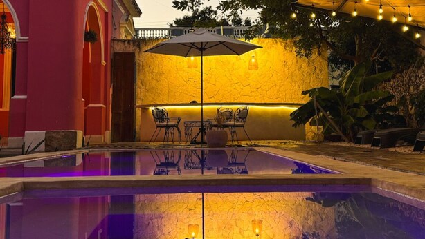 An outdoor pool area with a table and chairs, surrounded by a stone wall and plants. - La Casa Rosa Imperial (Mérida)