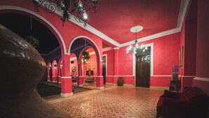 A hallway with red walls and patterned floor tiles, leading to a door with a dark wooden frame. - La Casa Rosa Imperial (Mérida)